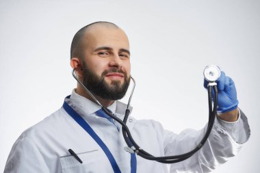 Mavi bir tıbbi eldivenin içinde elinde steteskop tutan mutlu bir doktor. Beyaz önlüklü ve mavi kravatlı sakallı bir doktor..