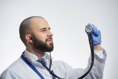 Steteskop takan mutlu bir doktor elindeki kafaya bakıyor. Beyaz önlüklü ve mavi kravatlı sakallı bir doktor..