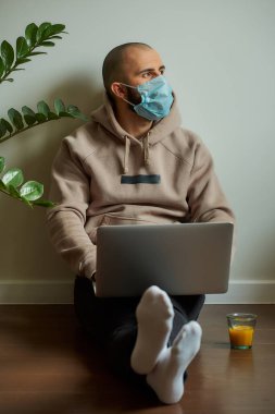 Uzaktan kumanda. Tıbbi maske takan bir adam karantina sırasında koronavirüsü yaymamak için uzaktan kumandayla çalışıyor. COVID-19 salgını sırasında evden eğitim gören kel bir programcı..