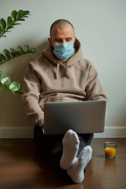 Uzaktan kumanda. Karantina sırasında dizüstü bilgisayarı üzerinde çalışan tıbbi yüz maskesi takmış bir adam. COVID-19 salgını sırasında evden çalışan kel bir programcı..