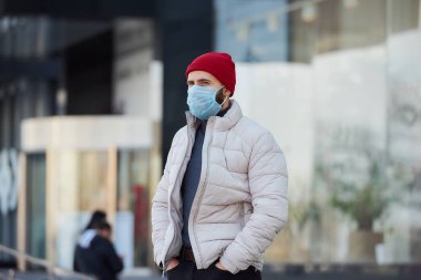 Yayılmış koronavirüsten (COVID-19) kaçınmak için tıbbi yüz maskesi takan beyaz bir adam. Yüzünde cerrahi maske olan bir adam sokakta kalıyor..