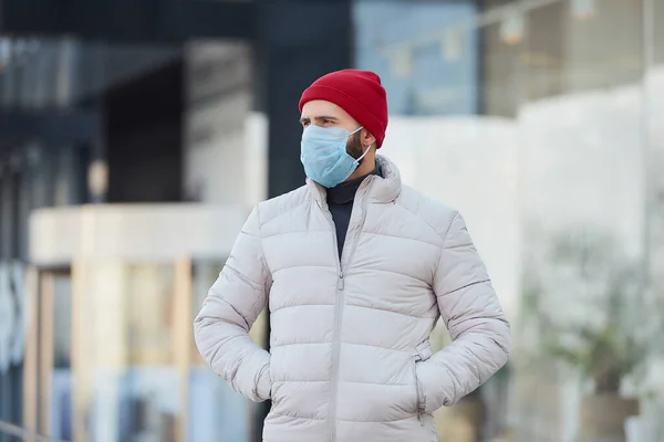 一个头戴医用口罩的高加索人 以避免扩散的头孢病毒 Covid 一个人脸上带着外科口罩因为大流行病在市中心等着他 — 图库照片