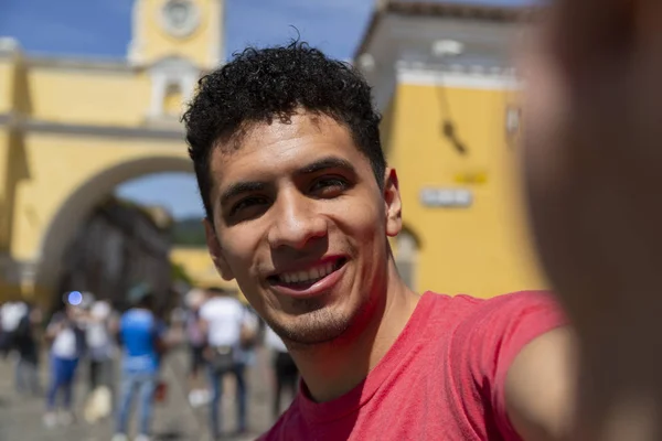 Young Hispanic man taking a self in the city of Antigua Guatemala with the Santa Catalina arch behind — Stock Photo, Image