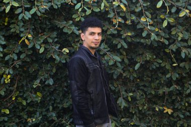 Yeşil yapraklardan oluşan bir duvarın içindeki İspanyol. Etrafı yapraklarla çevrili genç, şık bir esmer..