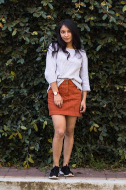 Arka planda yeşil yapraklardan bir duvarla gülümseyen İspanyol kadın. Doğayla iç içe gülümseyen zarif genç kadın.