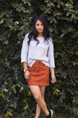 Arka planda yeşil yapraklardan bir duvarla gülümseyen İspanyol kadın. Doğayla iç içe gülümseyen zarif genç kadın.