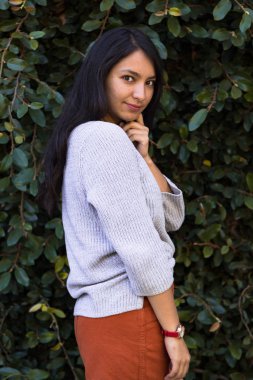 Arka planda yeşil yapraklardan bir duvarla gülümseyen İspanyol kadın. Doğayla iç içe gülümseyen zarif genç kadın.