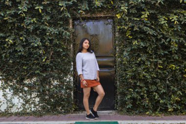 Arka planda yeşil yapraklardan bir duvarla gülümseyen İspanyol kadın. Doğayla iç içe gülümseyen zarif genç kadın.