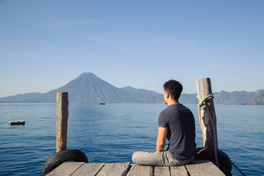 Guatemala 'nın mavi gölündeki turist Atitlan Gölü rıhtımında oturan genç İspanyol adam turizm cenneti.