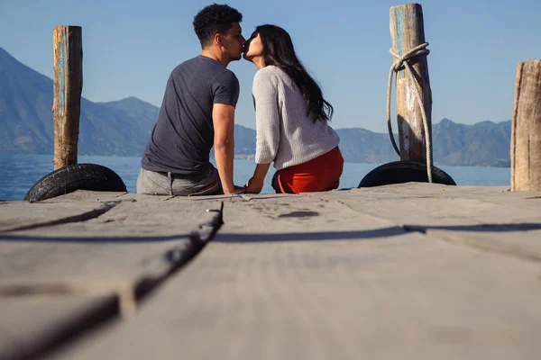 Kissing couple sitting on the pier of Lake Atitlan in Guatemala - traveling couple in tourist destination in Latin America