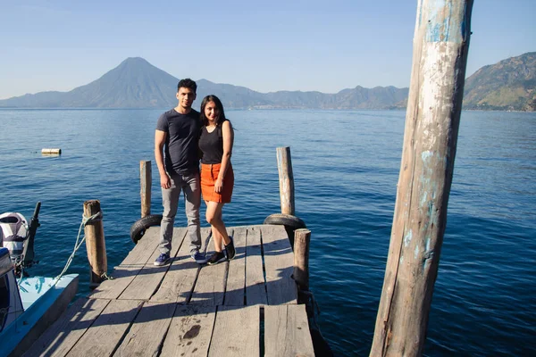 Traveling couple standing at the dock of Lake Atitlan smiling at the camera - sunrise on Lake Guatemala - Hispanic adventure couple in Latin America tourist destination