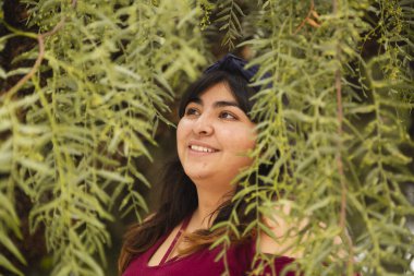 Ağaçların ortasında gülümseyen İspanyol kadın - doğal gülümsemenin ayrıntıları - Latin kadın