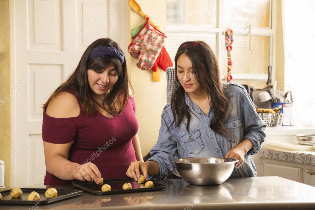 Hispanic sisters making chocolate chip cookies while having fun - women cooking homemade cookies - home activities