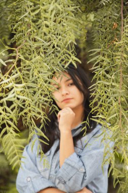 Ağaç dalları arasında kameraya bakan Latin kadının portresi.