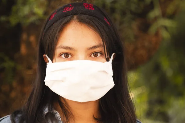 young woman wearing face mask on the street - Hispanic woman in nature wearing face mask