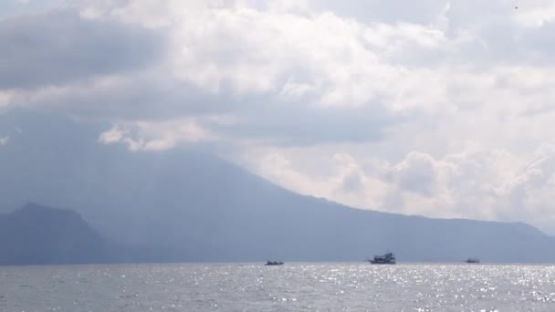 グアテマラのガテマラ湖の3つの遠くのボート火山や山に囲まれた海を航海する雲やボートと青い空の風景 — ストック動画