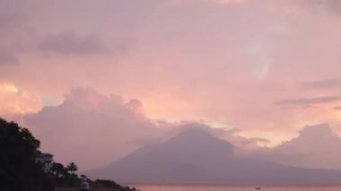 Guatemala 'daki temiz atitlan gölünde gün batımı. Gün batımında gölün ortasında küçük bir tekne. Gökyüzünde mor renkler olan bulutlar, volkanlar ve dağlar arasında.