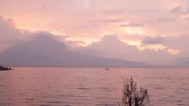 グアテマラの澄んだ大西洋の湖の日没雲火山山空に紫色の色の間の日没時に湖の真ん中の小さなボート — ストック動画