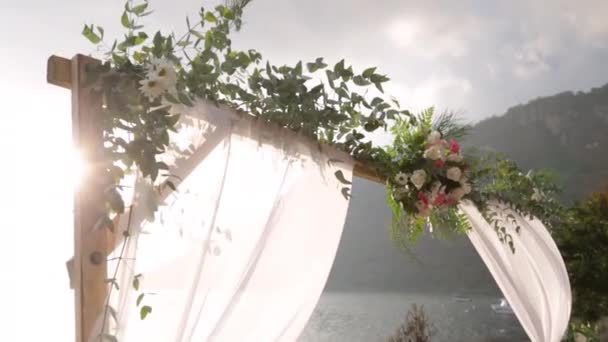 湖畔の結婚式の祭壇の上の花のアーチ日没時に山に囲まれた花の配置と自然結婚式の伝統 — ストック動画