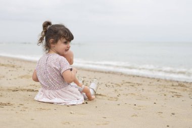 Kumsalda onu dolly ile oturan yürümeye başlayan çocuk