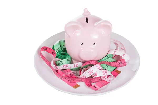 Pink piggy bank amongst tangled measuring tapes — Stock Photo, Image