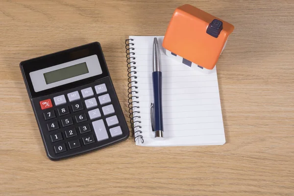 Calculadora, caneta e notebook e casa de brinquedo — Fotografia de Stock