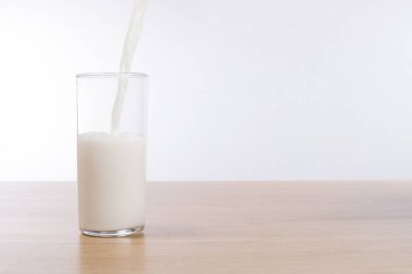 Fresh milk pouring into a glass on a bench top clipart