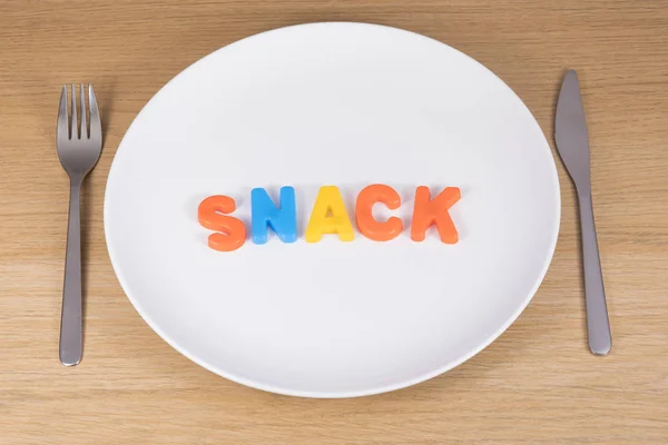 Een mes, een vork en een leeg bord met het woord snack — Stockfoto