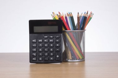 Hesap makinesi ile kap içinde renkli kalemler