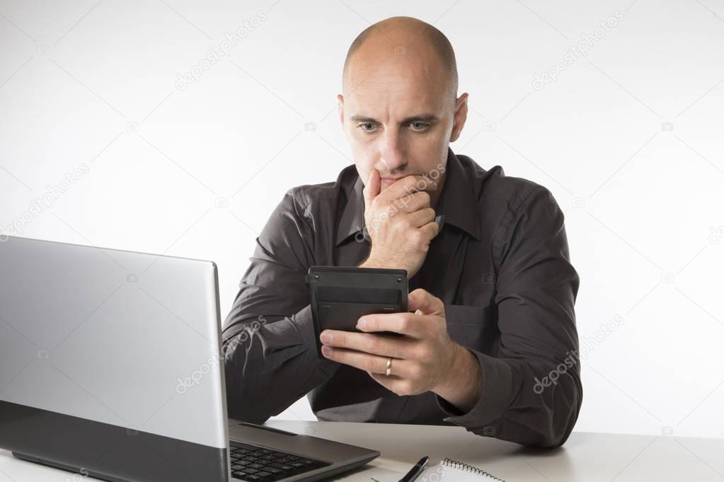 Worried man staring at a handheld calculator