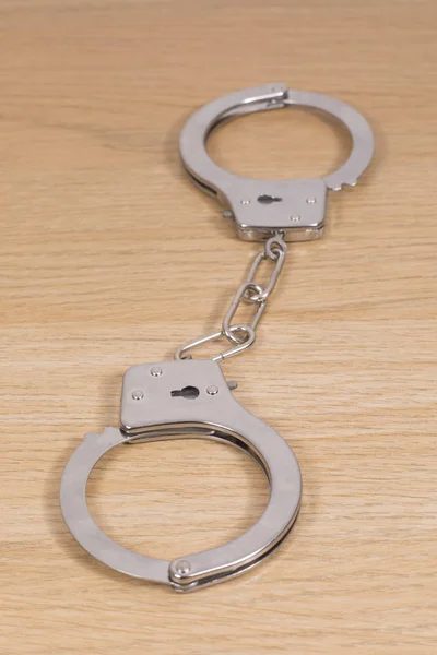 Pair of locked steel handcuffs on a wooden desk — Stock Photo, Image