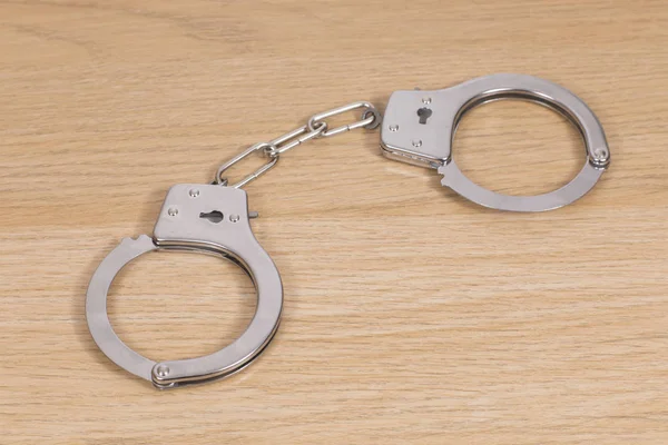 Closed handcuffs spread out on a wooden table — Stock Photo, Image