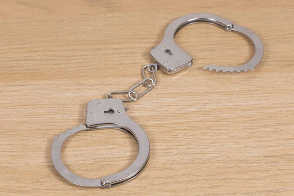 Handcuffs on wooden desk — Stock Photo, Image