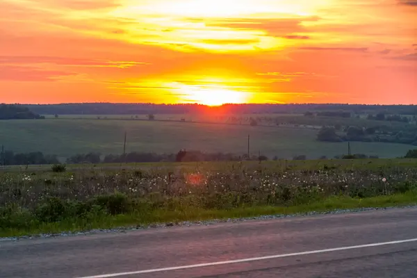 Puesta de sol detrás del campo agrícola con un cielo dramático naranja . — Foto de Stock