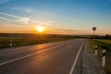 Tarım alanları üzerinde gündoğumu altında asfalt yol.