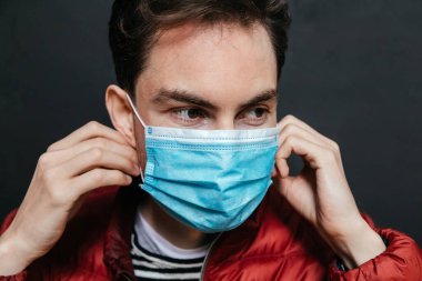 Siyah arka planda pandemik koronavirüsü önlemek için endişelenen, cerrahi maske takan çekici beyaz bir adamın portresi. Coronavirus Covid-19 konsepti. Sağlığınızı koruyun.