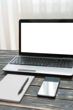 Ev işyerinde. Boş bir arkaplanda boş bir defter, dizüstü bilgisayar, kalem ve cep telefonu