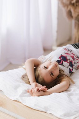 Beyaz elbiseli kahverengi saçlı çocuk sabah uyandıktan sonra beyaz gömlekli iç çamaşırları doğal ışıklandırmalı.