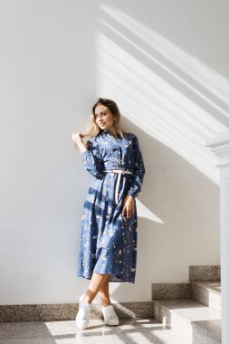 MIDI elbiseli genç, ince bir kız pencerenin kenarında güneş ışığının altında.