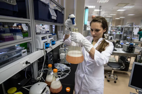 Mujer asistente de laboratorio con frasco en la mano en la bioquímica —  Fotos de Stock