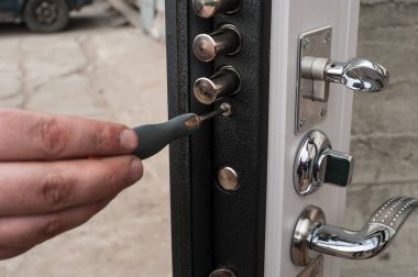 The carpenter installs a reliable burglar-resistant lock in the metal door. clipart
