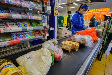 St. Petersburg, Rusya - 10 Nisan 2020: Süpermarket kasiyeri bir salgın sırasında müşterilere hizmet veriyor. Para makinesi. Satış makbuzu. Nakliye kaseti. Ürün
