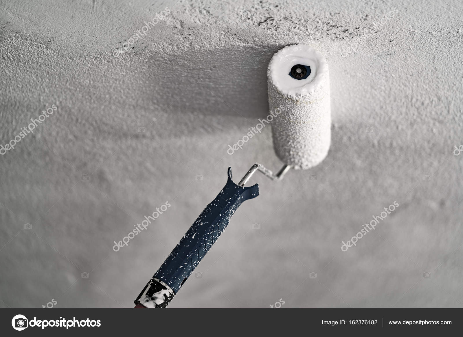 Roller With White Paint On A Concrete Ceiling Stock Photo