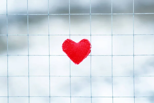 the symbol of love red knitted heart lying on metal bars of the