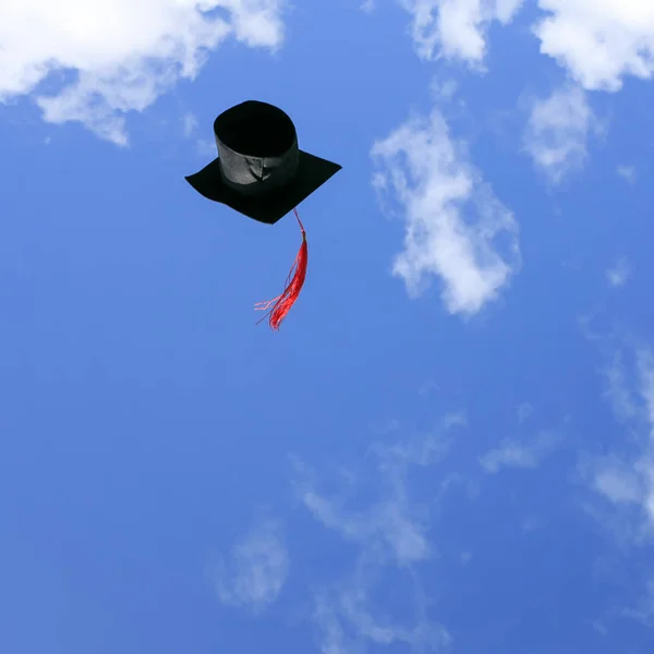 black student hat with red tassel soars high into the blue sky a