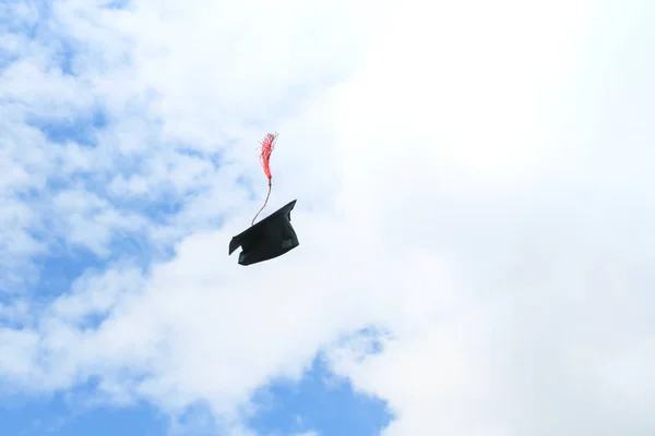 black student hat with red tassel tossed high in the blue sky on