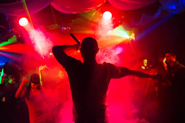 Silueta del hombre con un micrófono en el escenario en la discoteca bailando con multitud de gente divertida —  Fotos de Stock