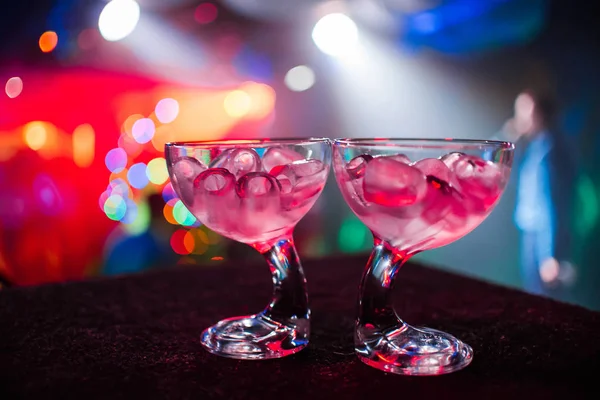 Stylish glasses with ice at party with colorful blurred background — Stock Photo, Image
