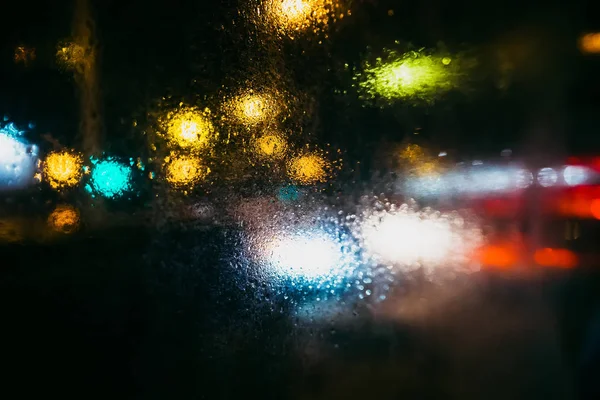 Rain drops on glass with blurry background of city at night with colored lights from street lamps and cars — Stock Photo, Image