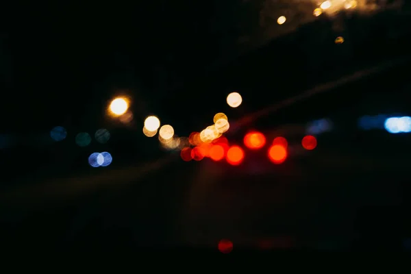 Luces borrosas de la ciudad y bokeh rojo a través del cristal del coche en la carretera por la noche — Foto de Stock